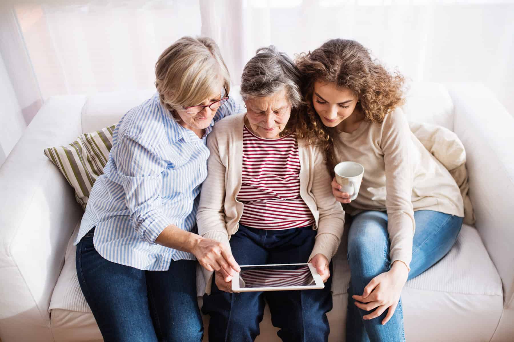 A Teenage Girl, Mother And Grandmother With Tablet At Home.